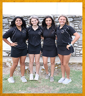 Four students lined up in front of rock wall